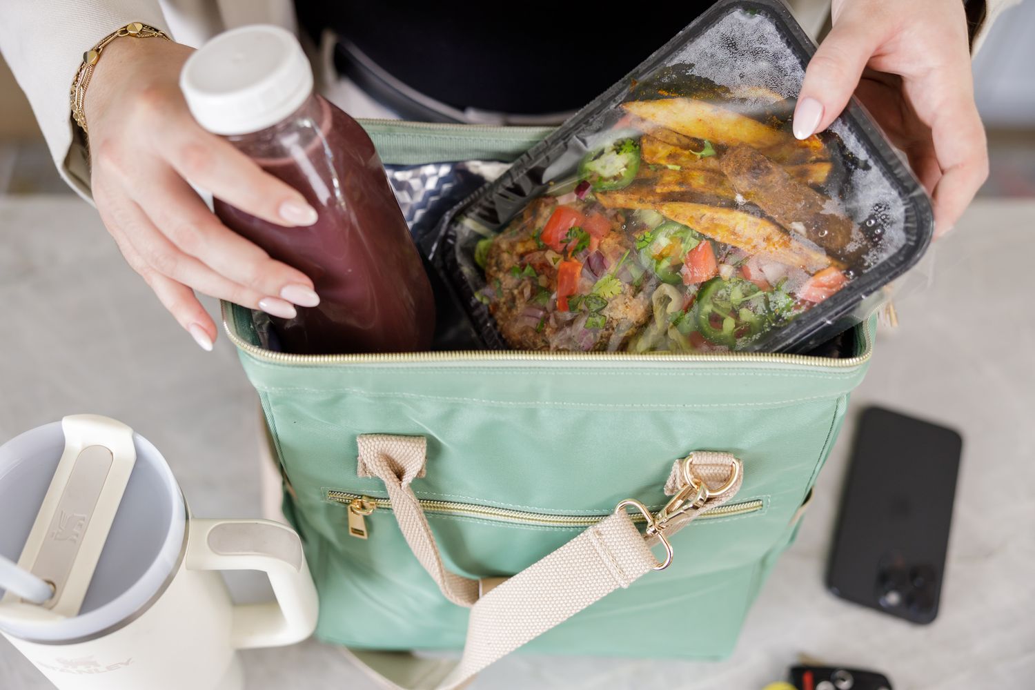 meal prep service in Seattle, WA woman hands placing sealed meal in cooler bag with beet juice on counter water bottle and phone product