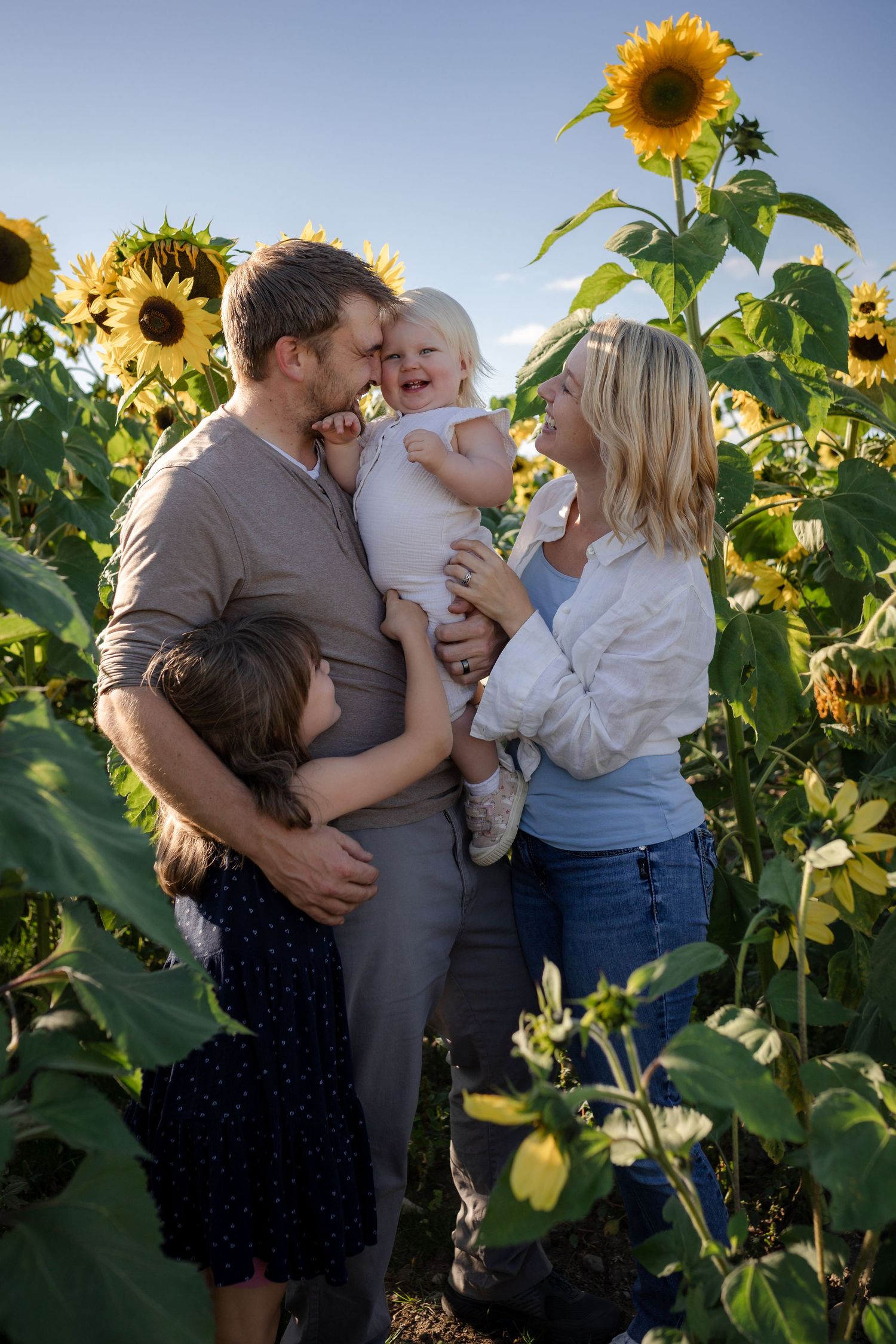 a blond woman holding a camera in a green field with daffodils and holding a camera while a little girl in pink gives her a big hug.