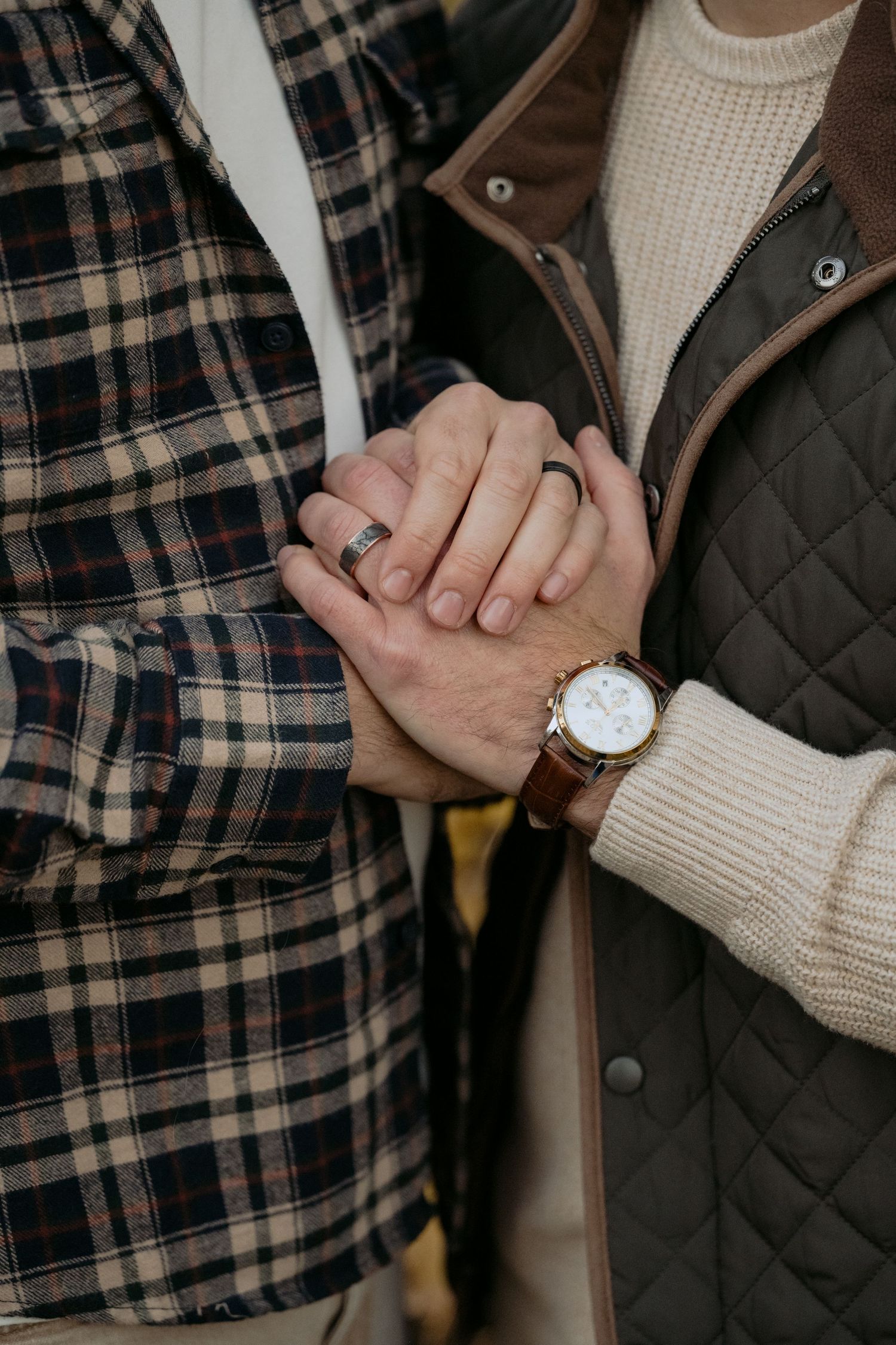 Gay couple holds hands to show off their engagement/wedding bands for an outdoor Fall engagement session in Stillwater, MN.