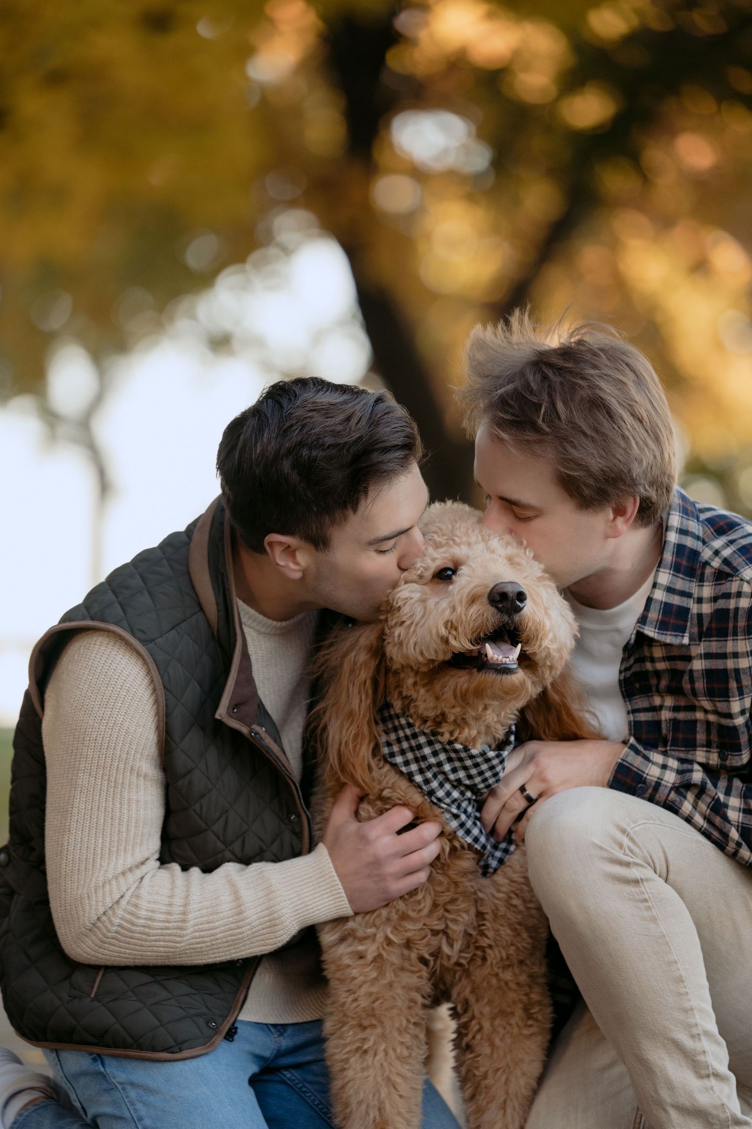 Engaged gay couple kisses their dog during a Fall outdoor engagement session in Stillwater, MN.