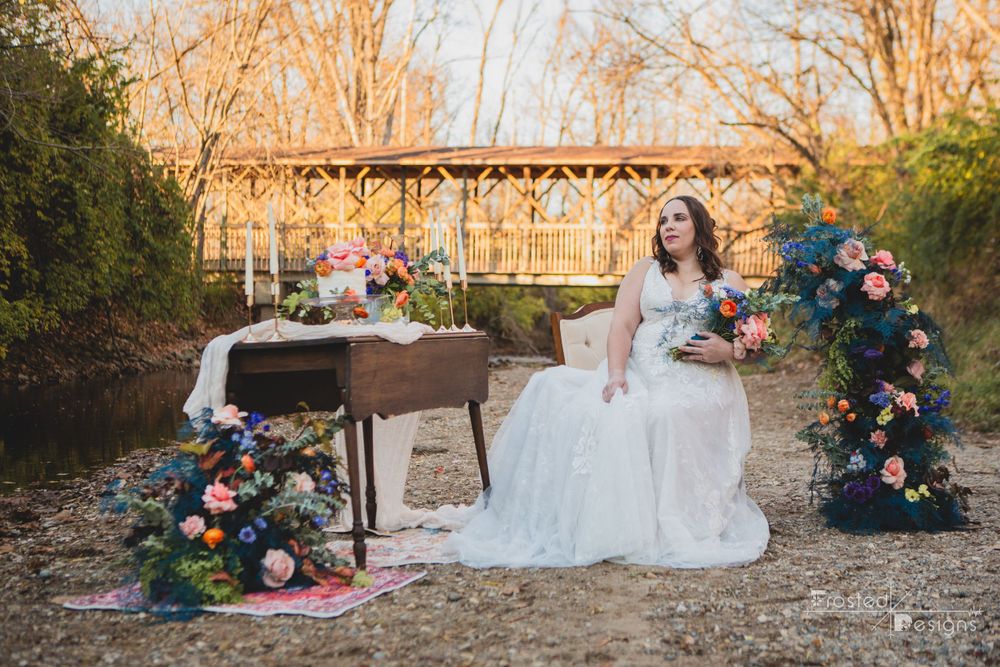Bridal Portrait Outdoors in front of a covered bridge with flowers, table, cake and candles.