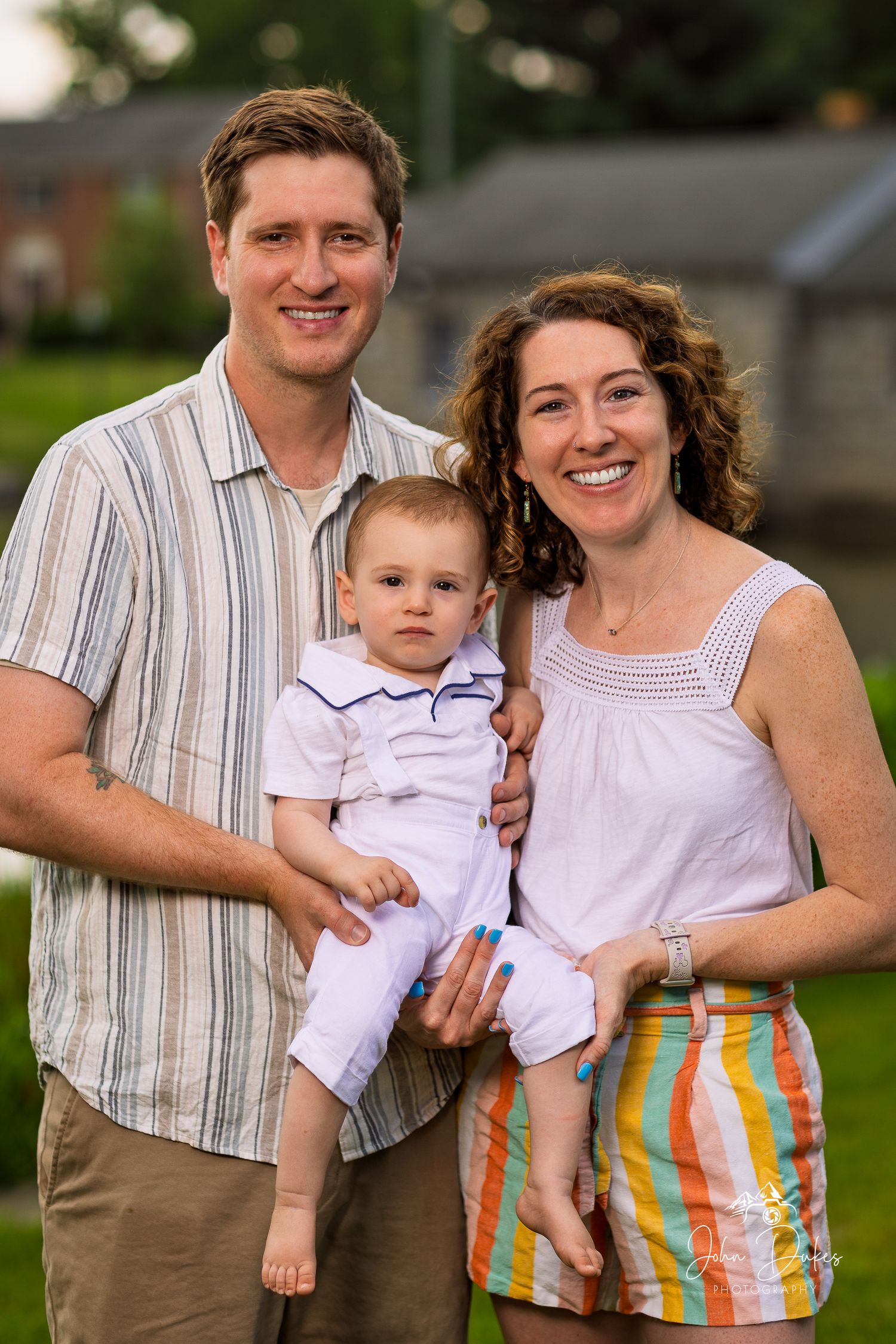 A family of three poses together outdoors in casual summer attire.