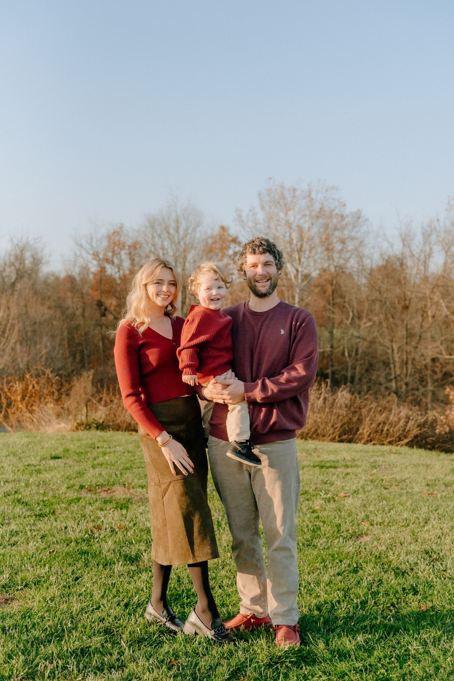Family portrait session in a sunny autumn field with warm burgundy and purple outfits.