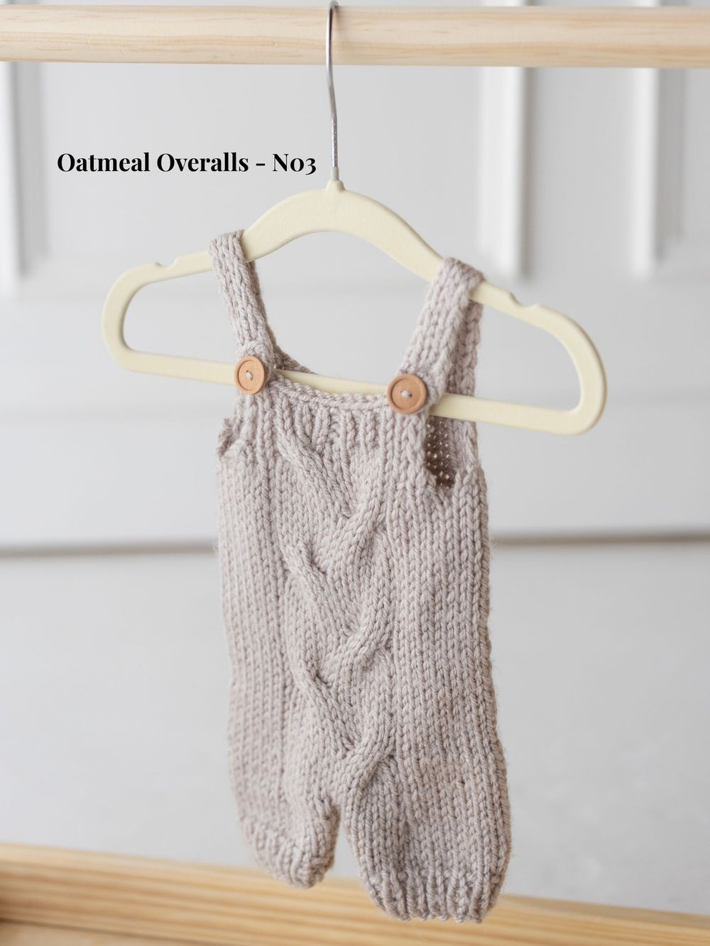 Gray knitted baby overalls with wooden buttons displayed on multiple hangers against a white background.