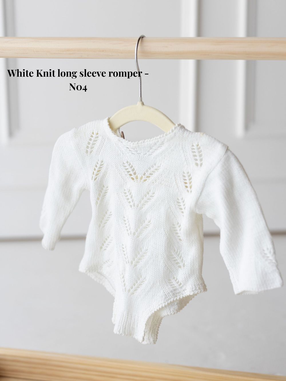 White knit long sleeve baby romper displayed on hangers showing different angles of the delicate pattern details.