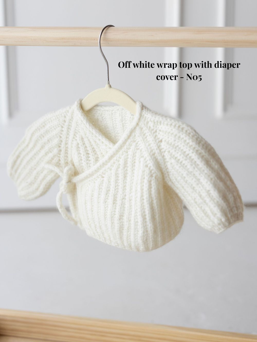 White knitted baby cardigan with ribbed pattern and button closure displayed on a hanger against a light background.