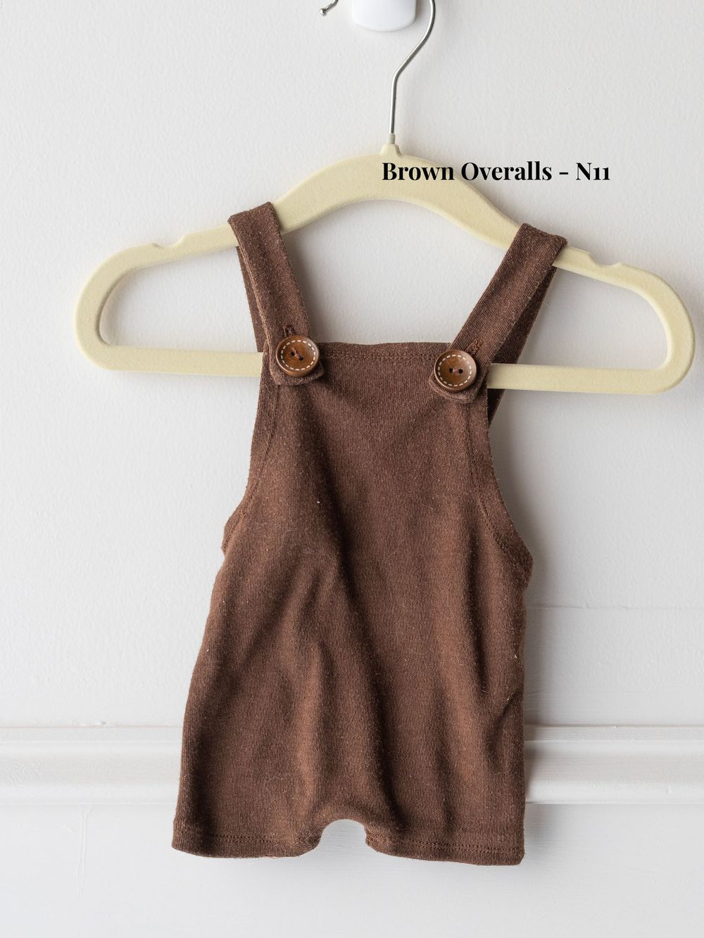 Brown corduroy baby overalls on a white plastic hanger against a light background.