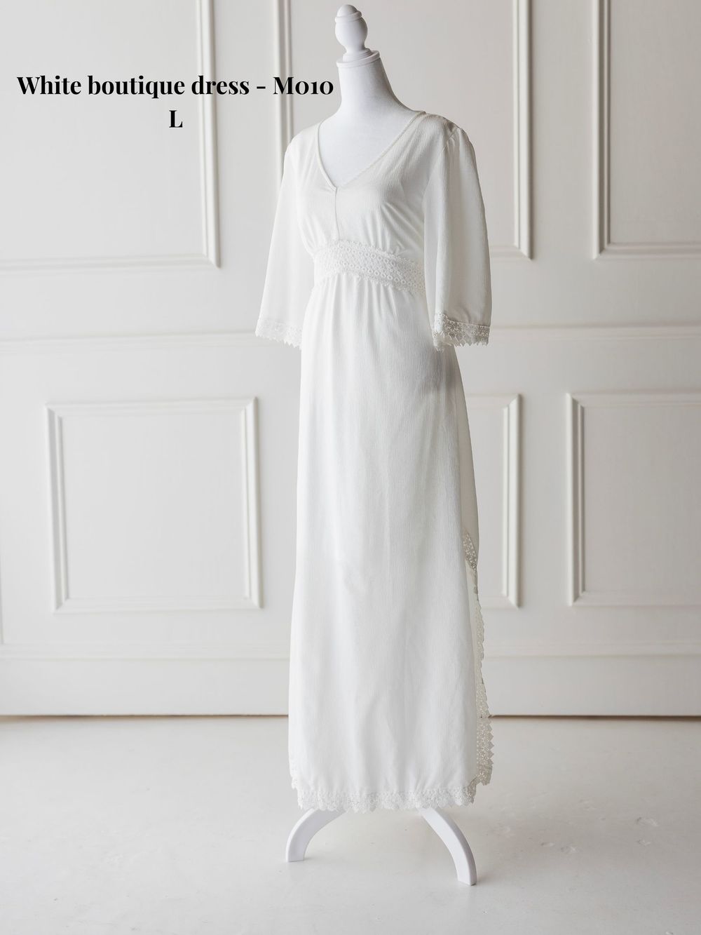 Classic white boutique dress with fitted bodice and flowing skirt displayed on mannequin against white wall.