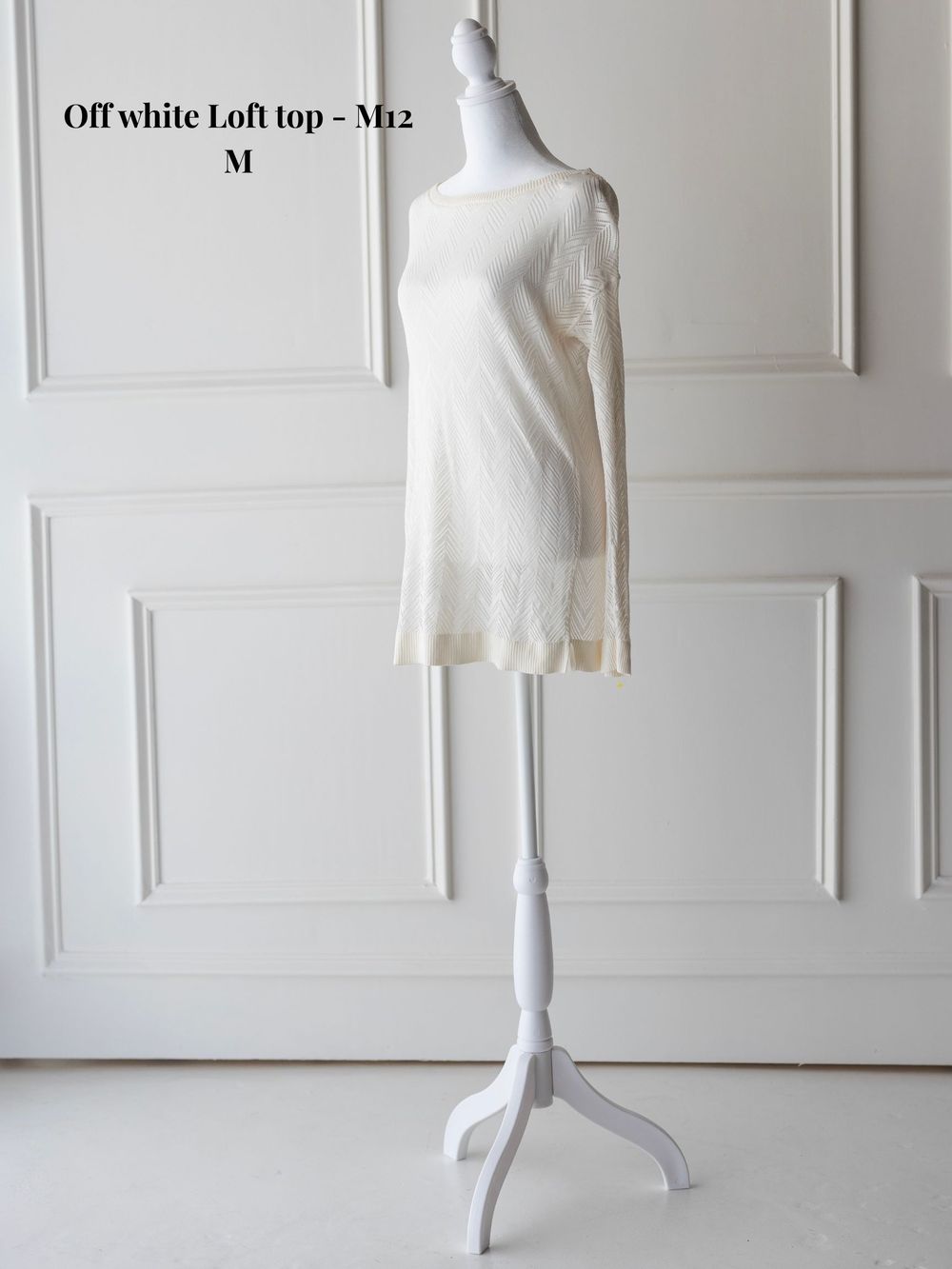 Off-white loft top with sleeveless design displayed on mannequin against white paneled wall.