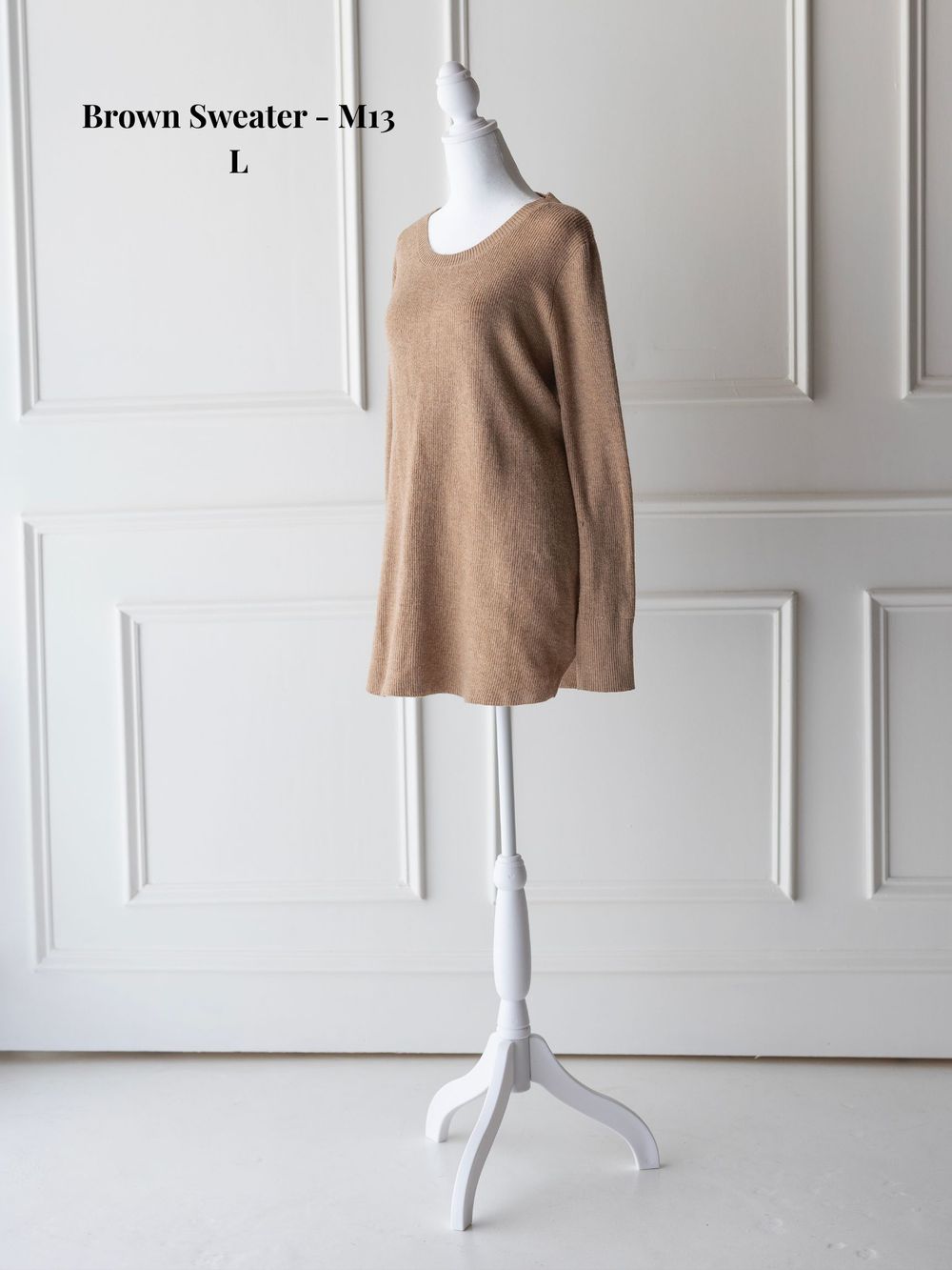 A brown knit sweater displayed on a white mannequin form against a light gray paneled wall background.