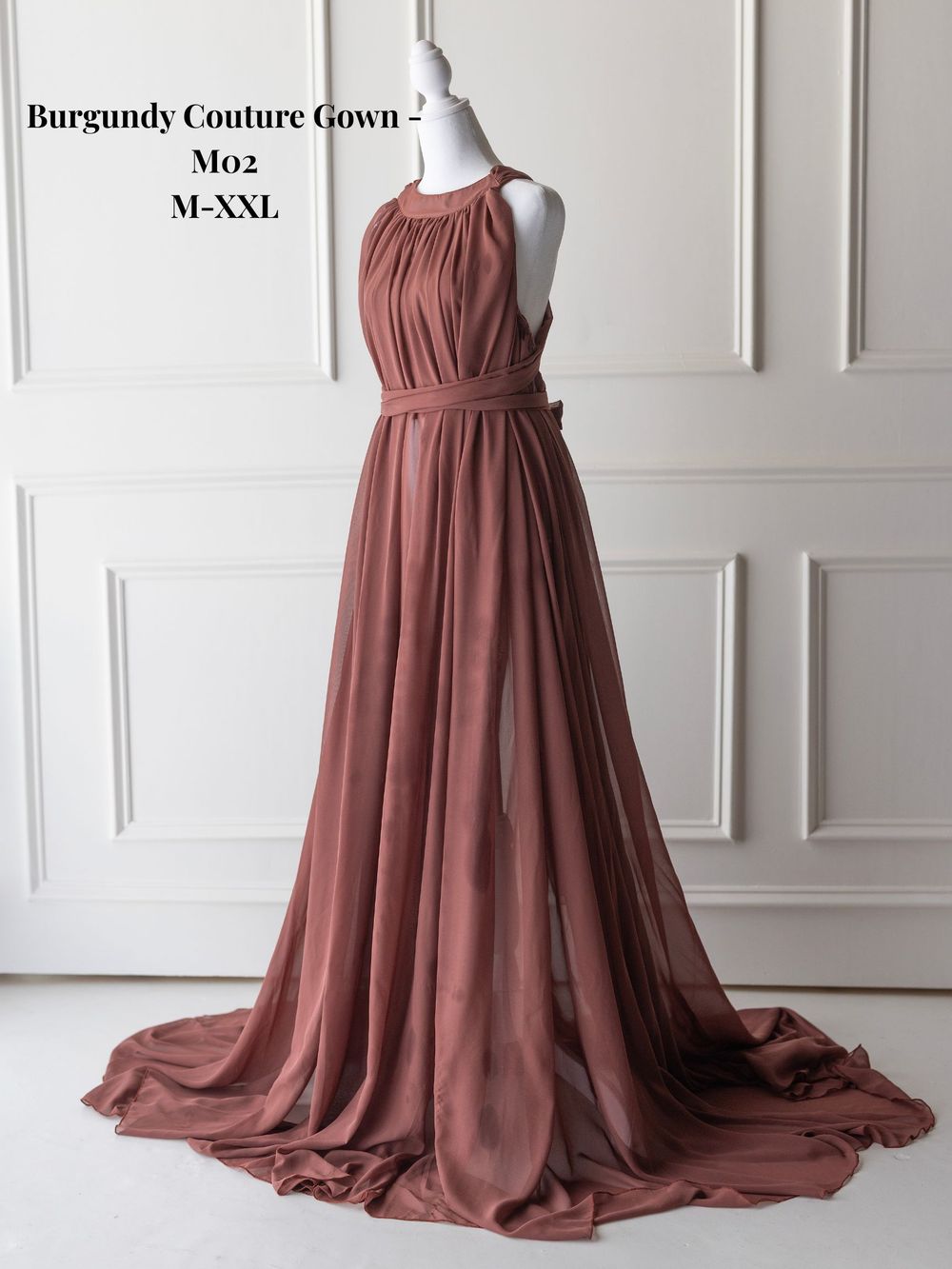 Elegant burgundy chiffon couture gown with gathered bodice and flowing train displayed on mannequin against white wall.