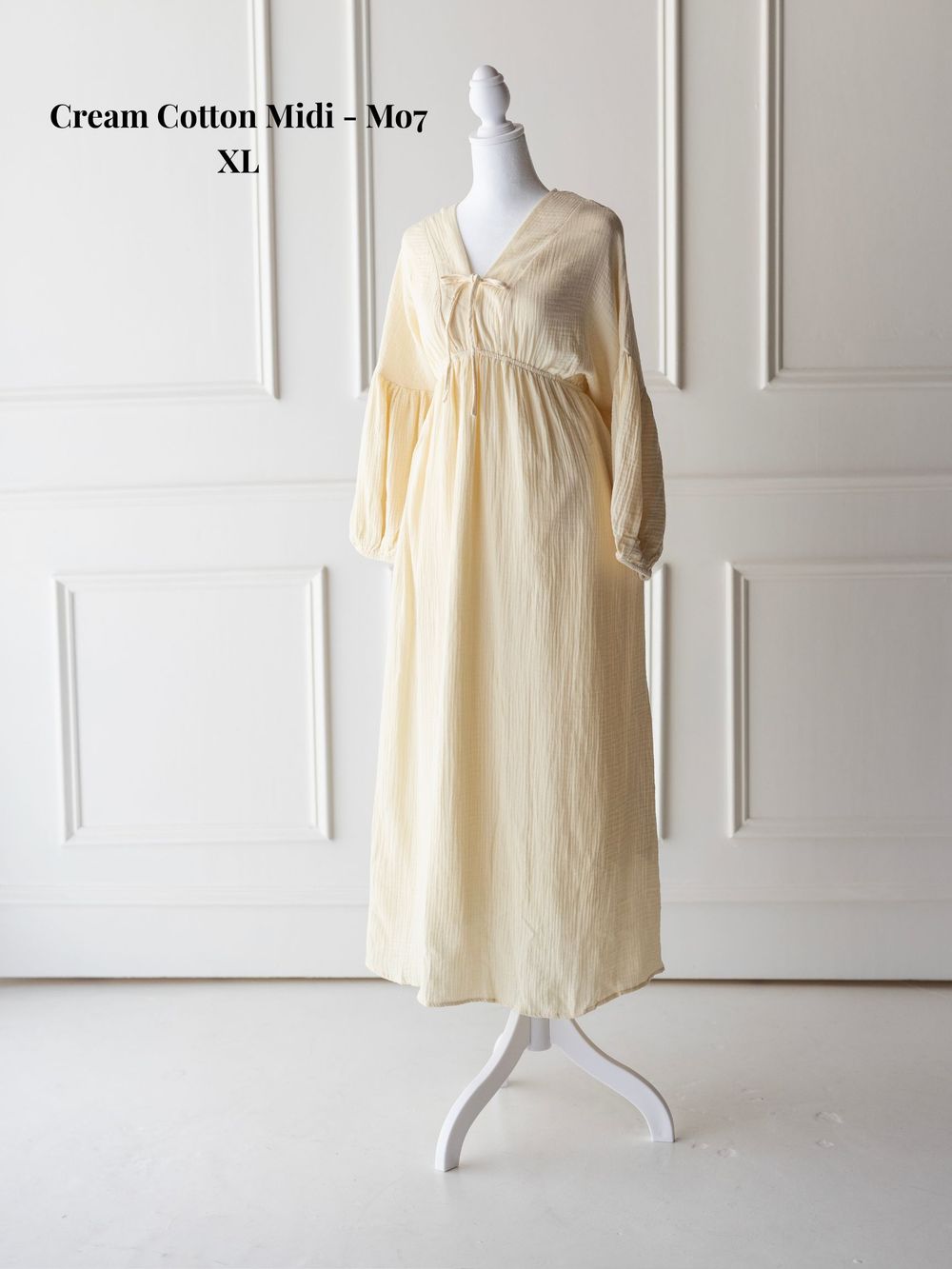 Cream colored cotton midi dress with loose fit and sleeveless design shown on dress form in studio setting.