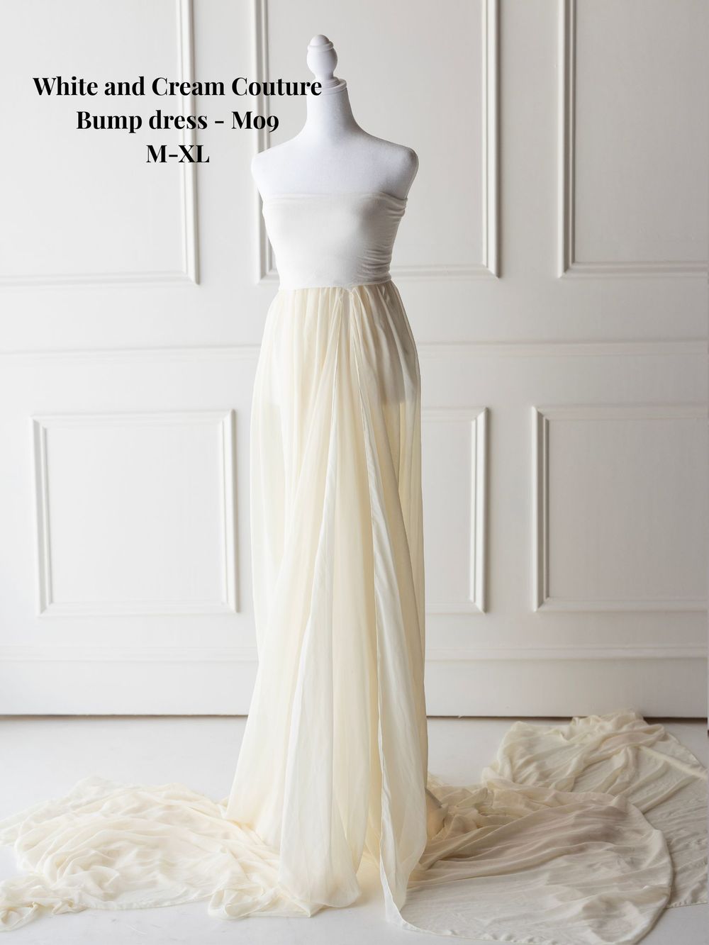 Cream and white strapless couture gown with flowing skirt shown on dress form against white wall backdrop.