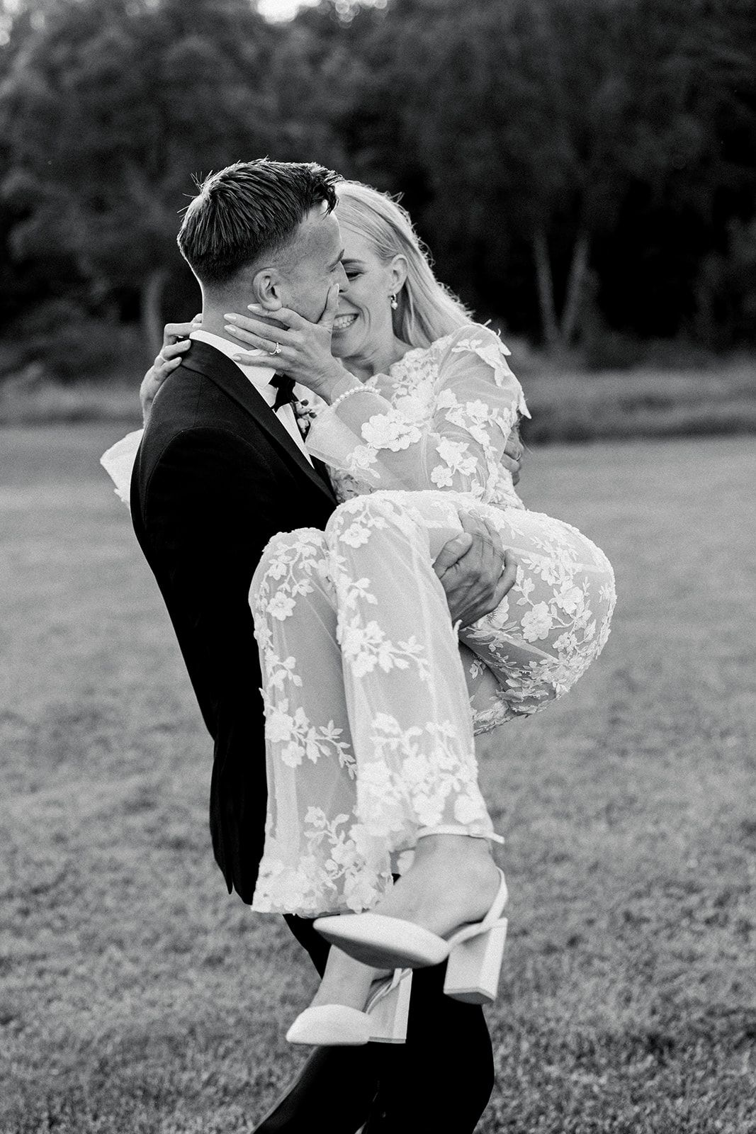 A couple in wedding attire embraces and kisses in a romantic black and white outdoor portrait series.