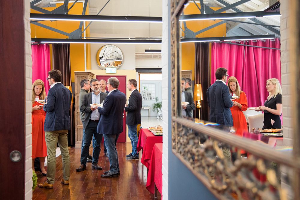 People gathered at an indoor event space with red curtains and yellow walls for a social function.