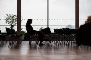 Empty cafeteria interior with silhouetted chairs and tables against large windows during daytime.