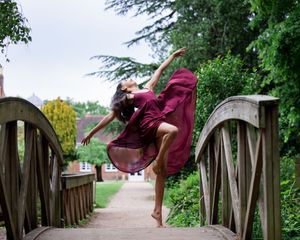A ballet dancer striking a post on a rustic wooden bridge surrounded by lush green gardens.