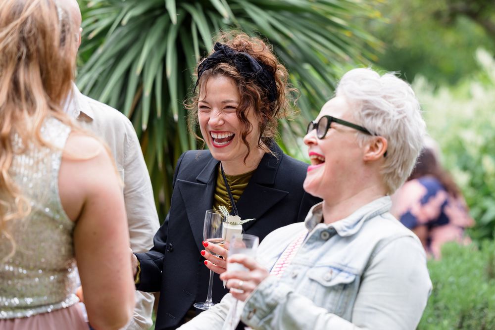 Wedding guests enjoying drinks and laughter during an outdoor garden reception celebration.