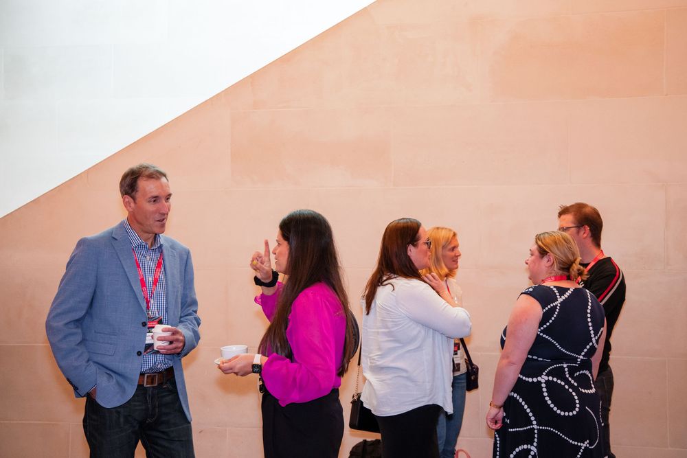 A group of business professionals networking and socializing at a corporate event against a peach-colored wall.