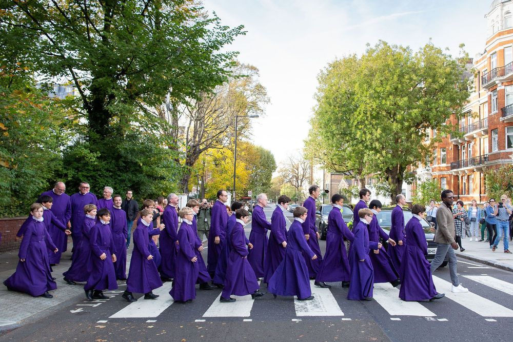 Group wearing purple graduation gowns walks across Abbey Road in London recreating the famous Beatles album cover.