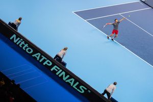 Tennis player serves the ball on a blue hard court during an indoor match.