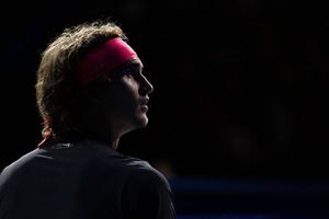 Silhouetted tennis player wearing a red headband looks upward in dramatic lighting against dark background.