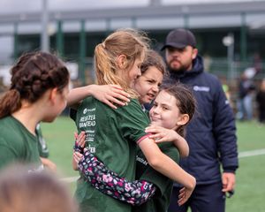 Athletes in green uniforms share an emotional embrace on a sports field during what appears to be a team moment.