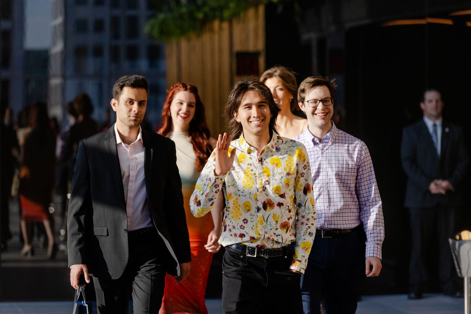 Business professionals walking through an office hallway with modern glass walls and natural lighting.