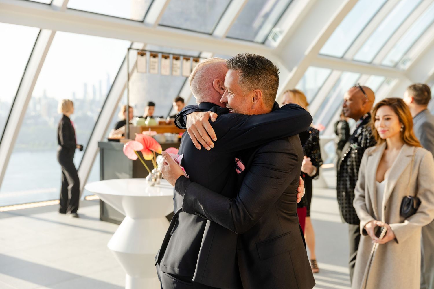 People embrace and congratulate each other in a bright, modern office space with angled glass windows.