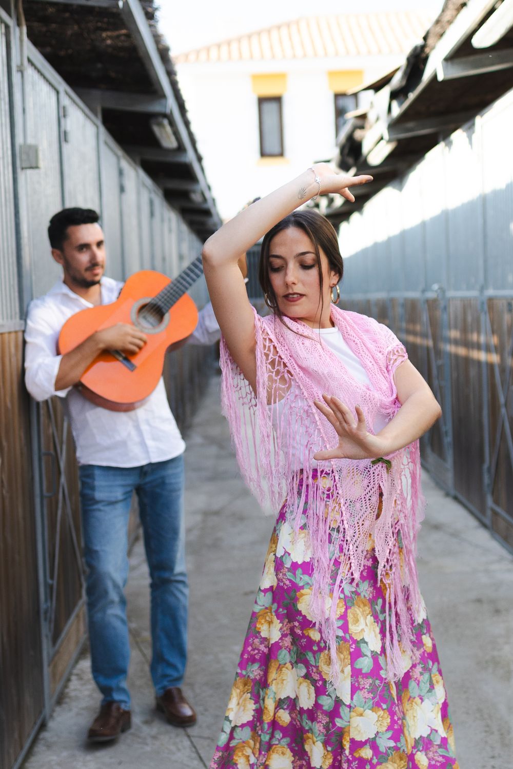 Flamenco dancers in colorful dresses perform while a guitarist plays in the background on a wooden porch.