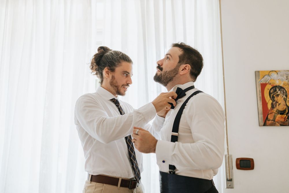 Two people in formal white shirts and black ties help each other adjust their neckwear before an event.