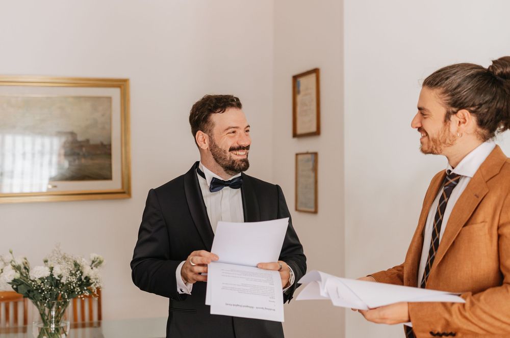 Two professionals in business attire sharing a laugh while reviewing documents in a bright office setting.