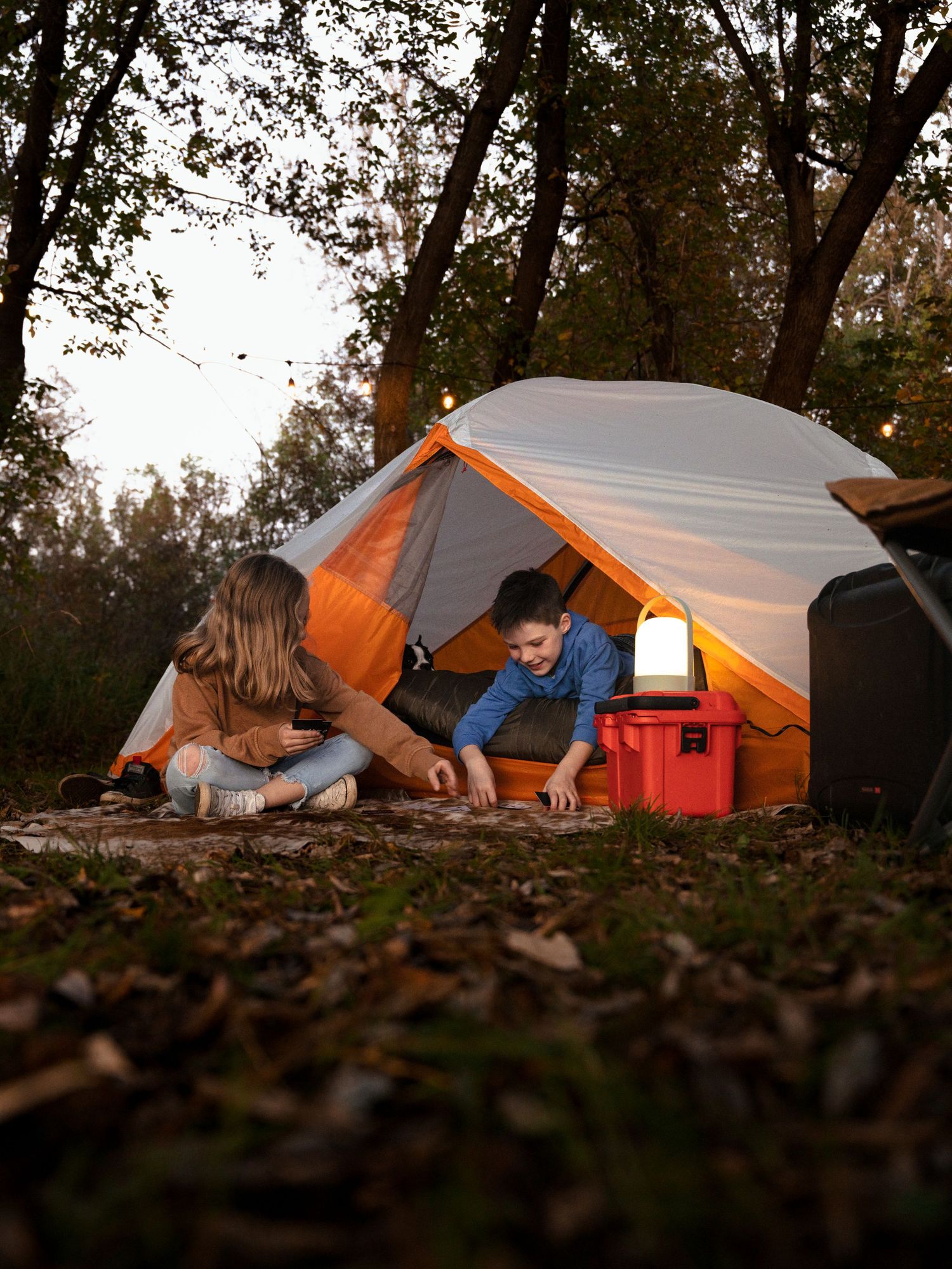 Row of orange and white tents set up among fallen leaves at dusk.