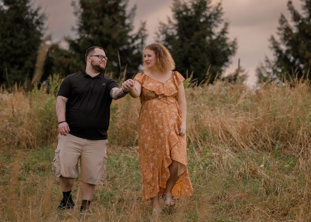 Couple in casual attire walking through a grassy field during golden hour.