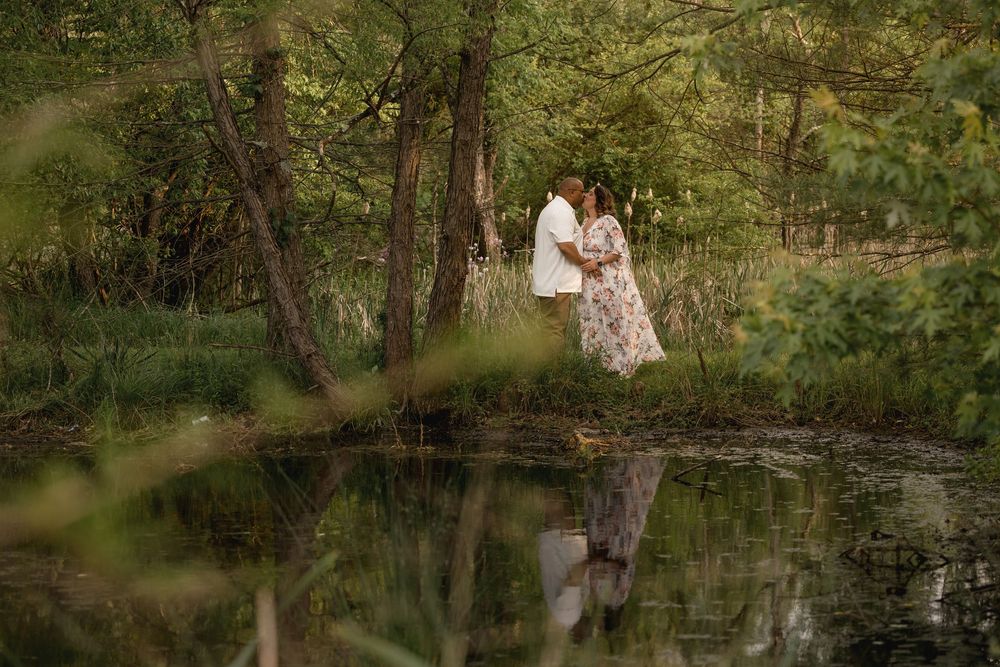 Couple walking together near a scenic pond surrounded by trees and greenery.