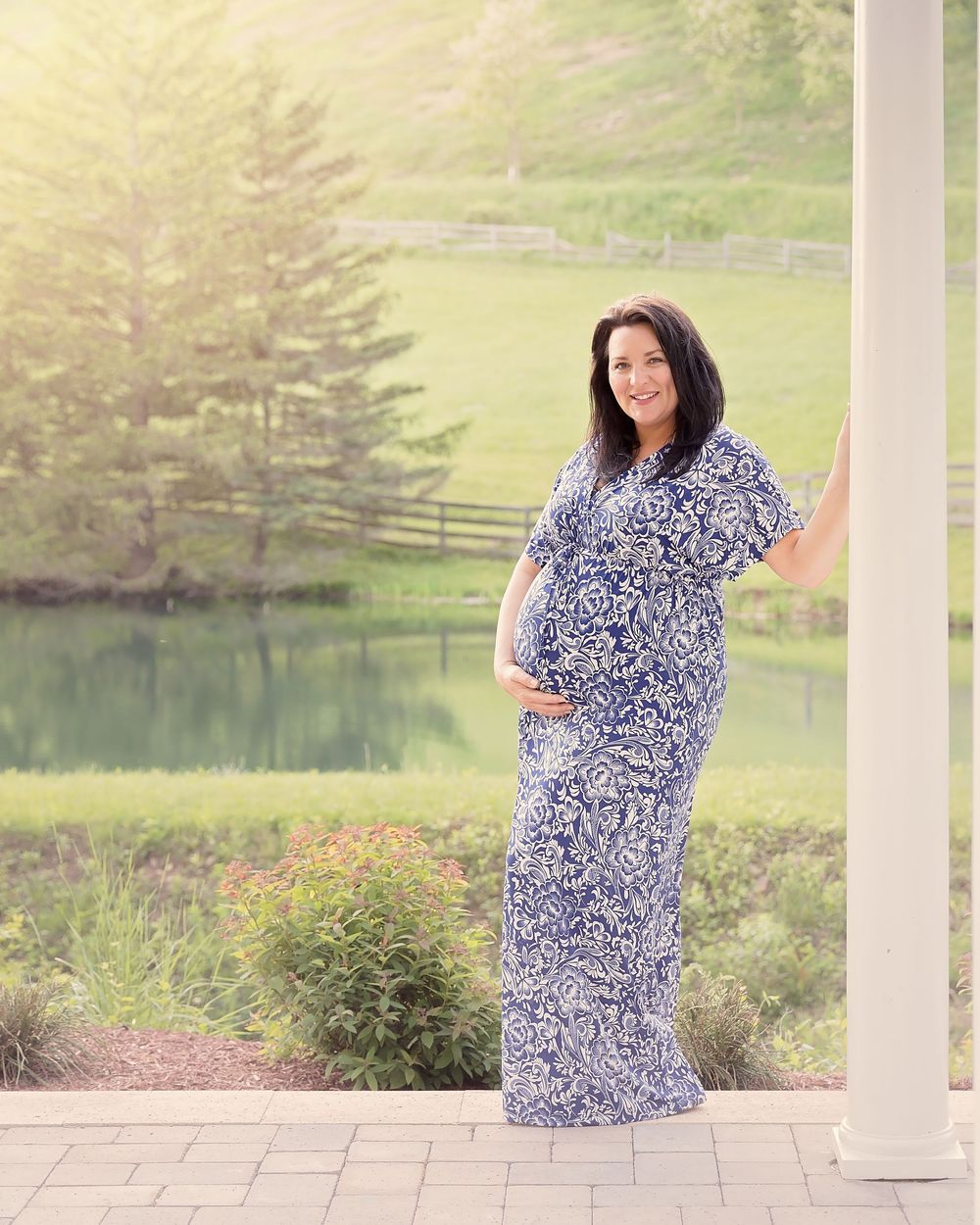 Person in a blue and white patterned dress posing on a porch overlooking a scenic landscape.