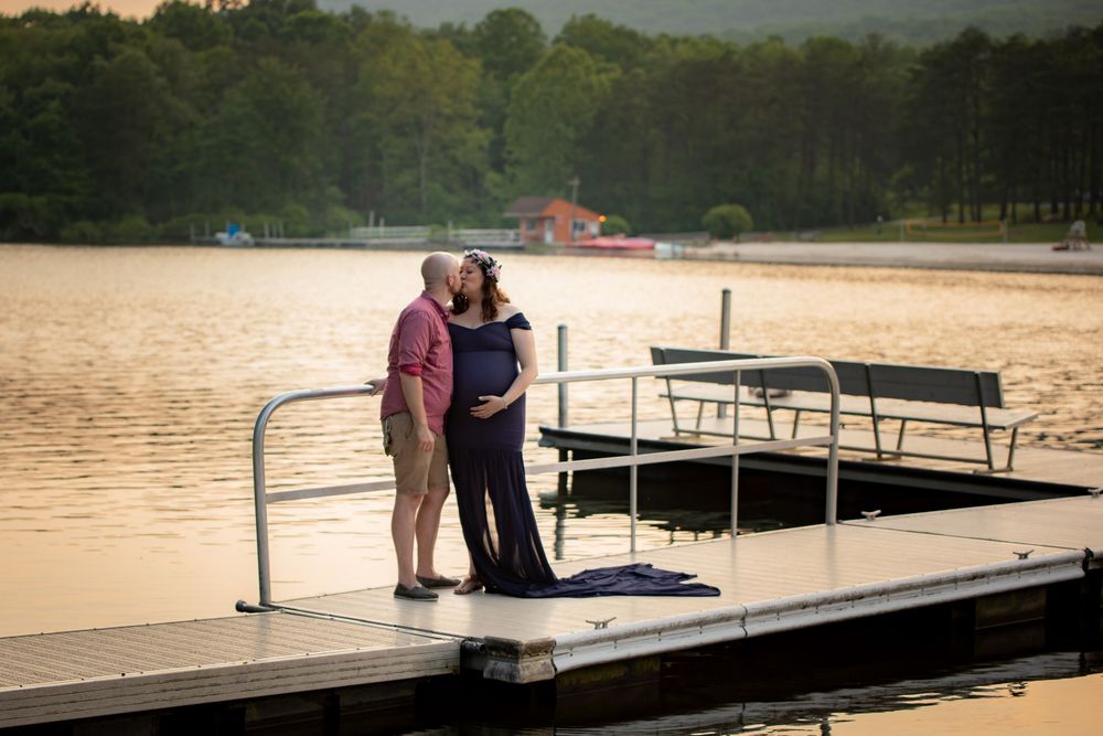 Couple standing together on a wooden dock by a serene lake at sunset.