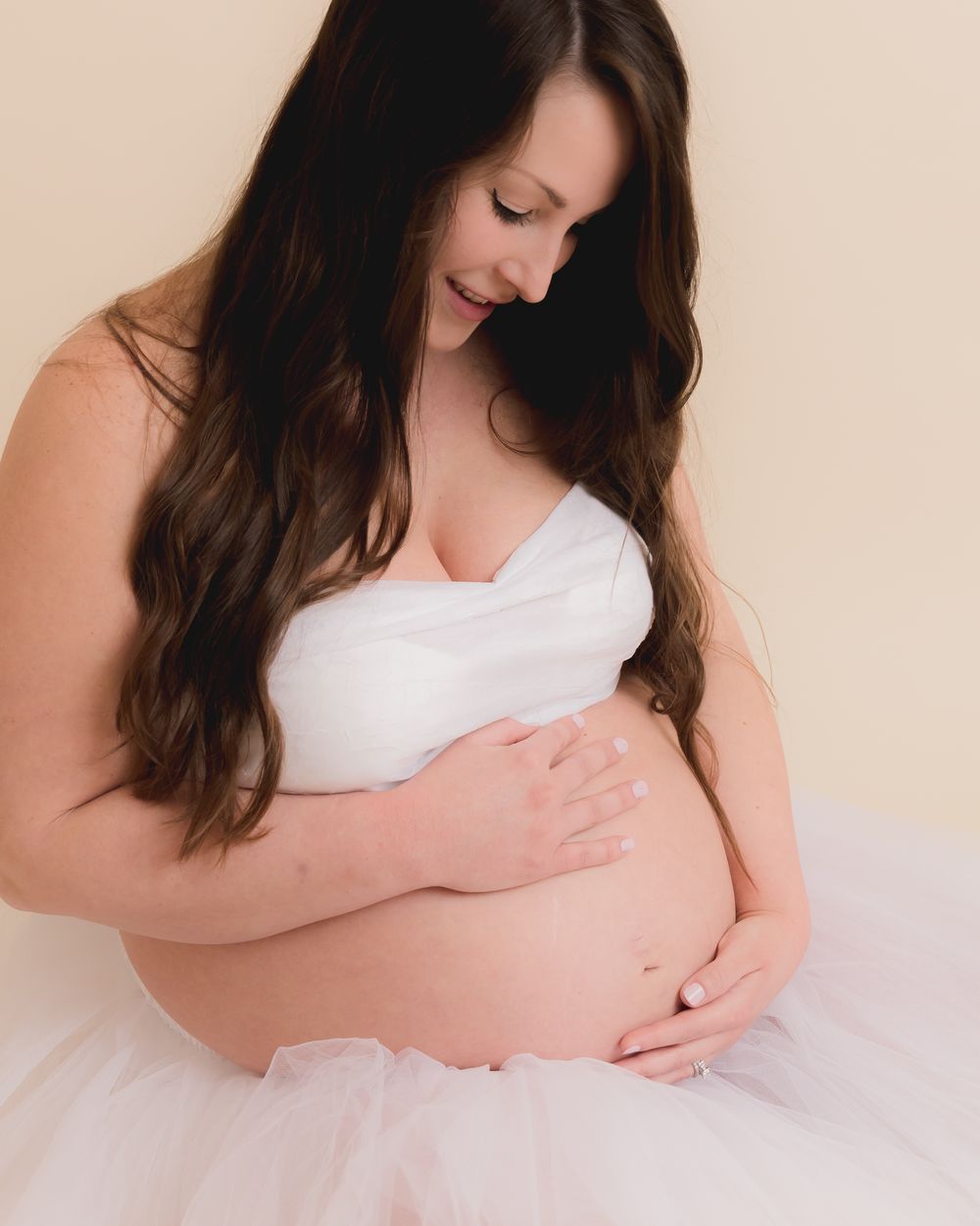 A maternity portrait featuring a white tulle dress against a neutral background.