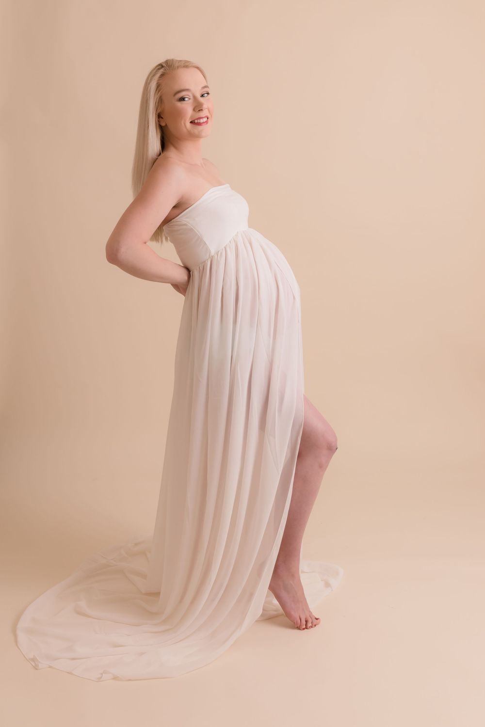 A maternity photo showing an elegant pose in a flowing cream-colored gown.