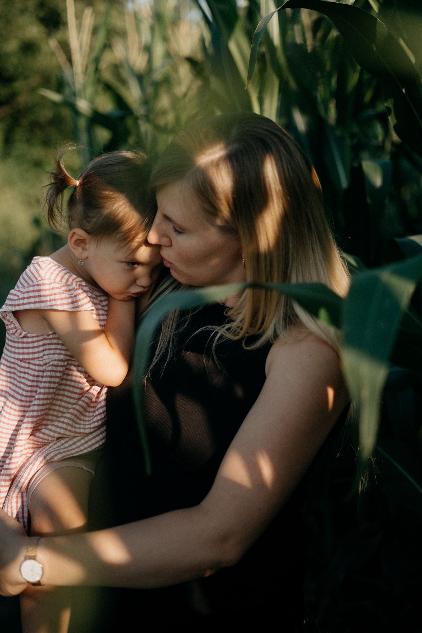 Intimate family moment captured in dappled sunlight through leaves.