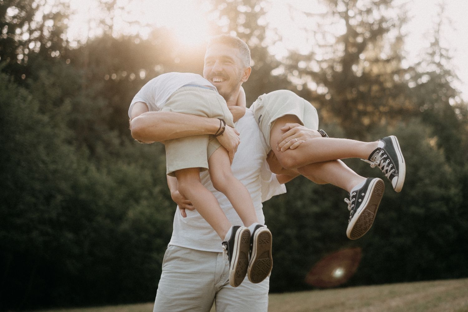 A playful moment captured at sunset with someone holding children upside down in a park setting.