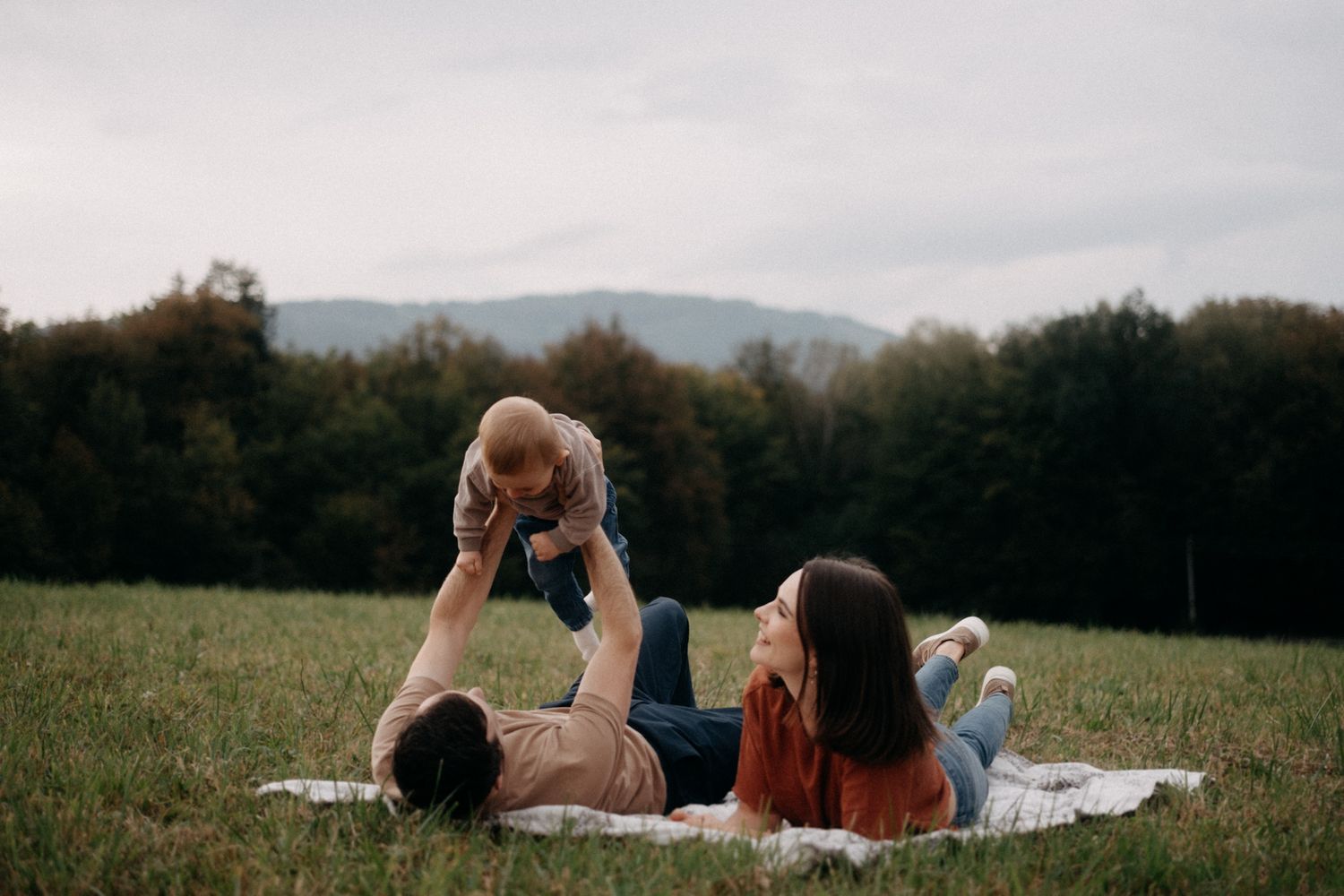 Family relaxes together on a picnic blanket with mountain views in background.