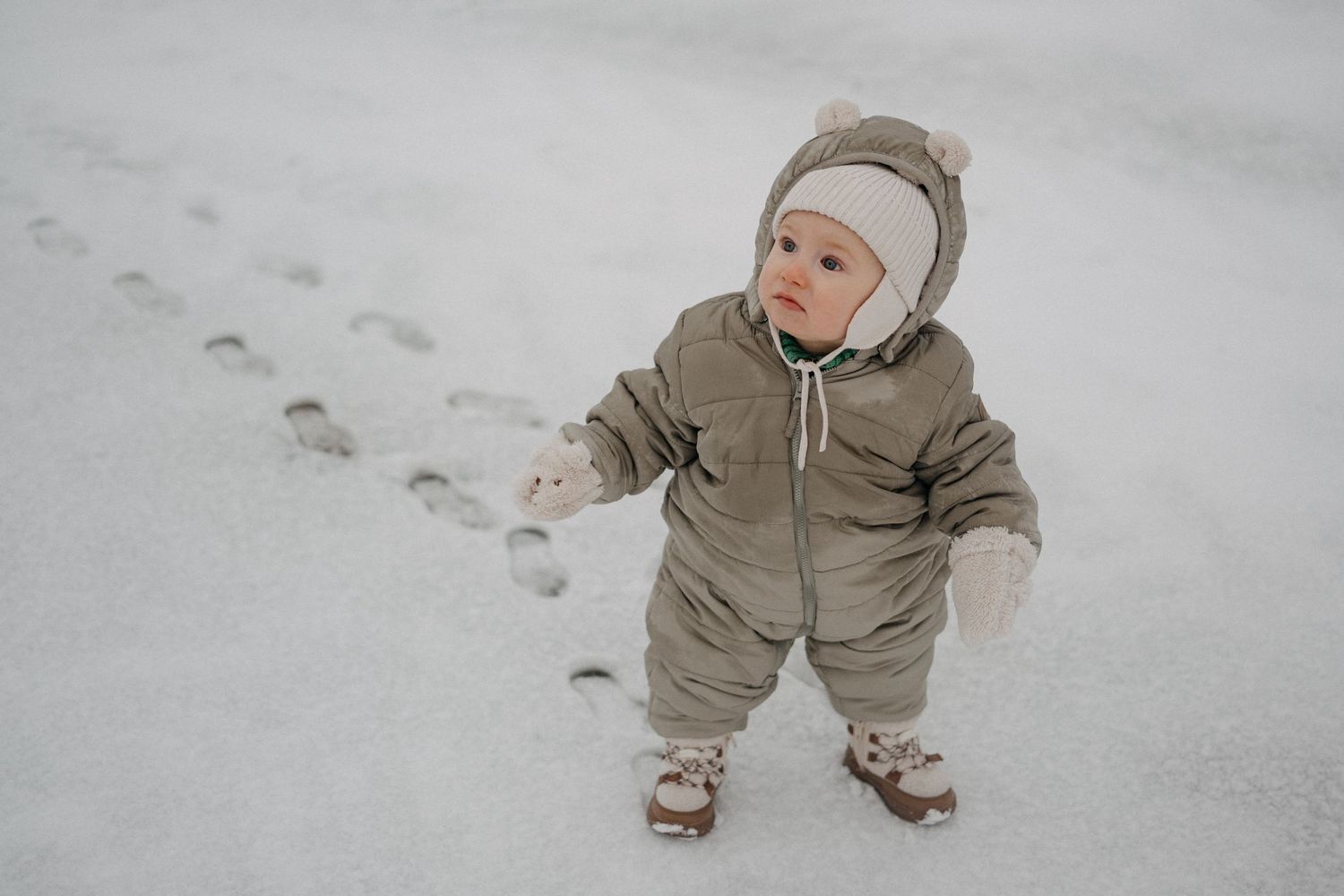 Small child bundled in winter clothing crawls through fresh snow.