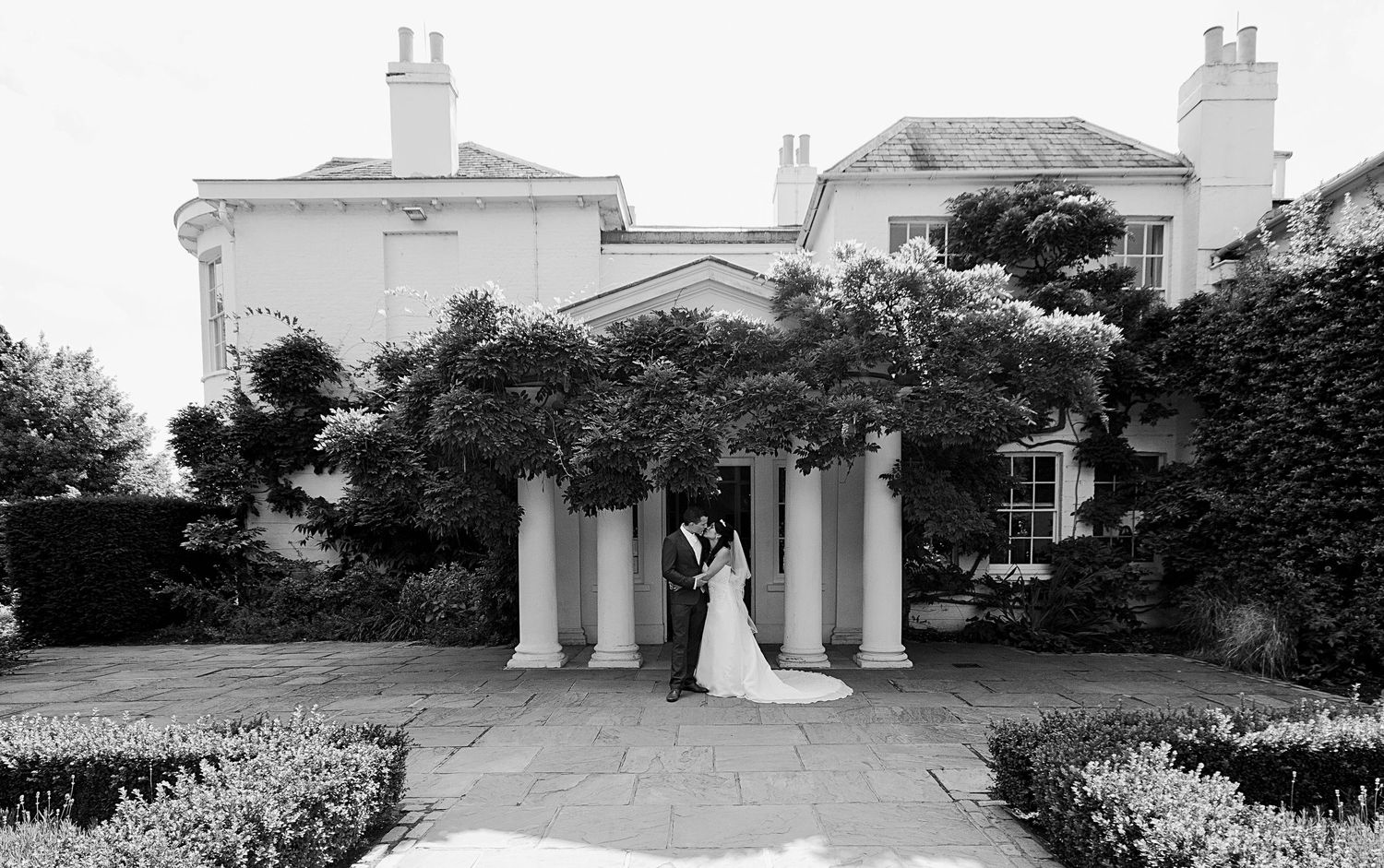 A panoramic black and white photo sequence showing the exterior of a stately mansion with columns and landscaped gardens.
