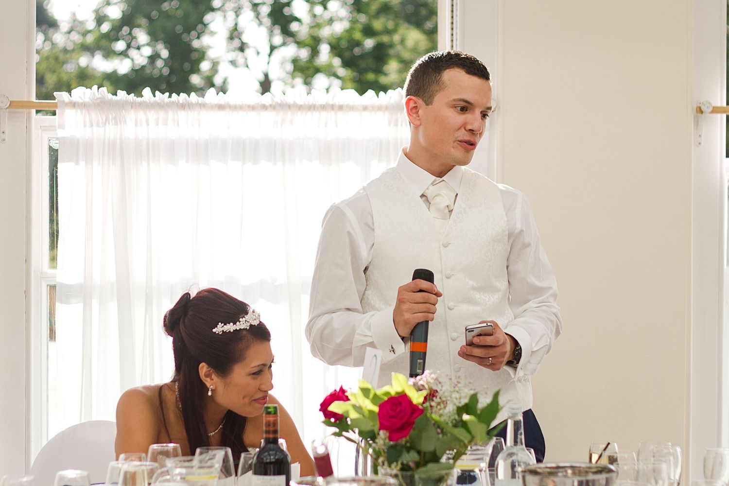 A group of wedding guests sit at an elegant reception table with white linens and floral centerpieces.