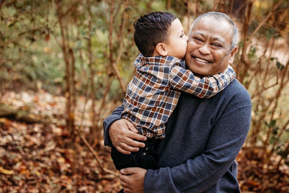 A heartwarming moment shared between a grandfather and young grandson embracing outdoors among autumn foliage.