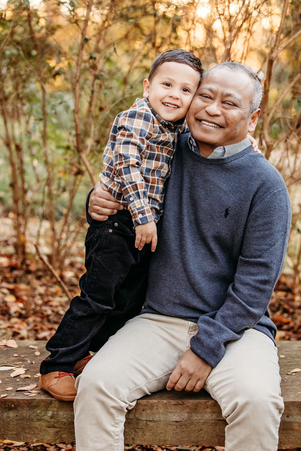 Two people share a warm embrace while sitting on a wooden bench surrounded by autumn foliage.