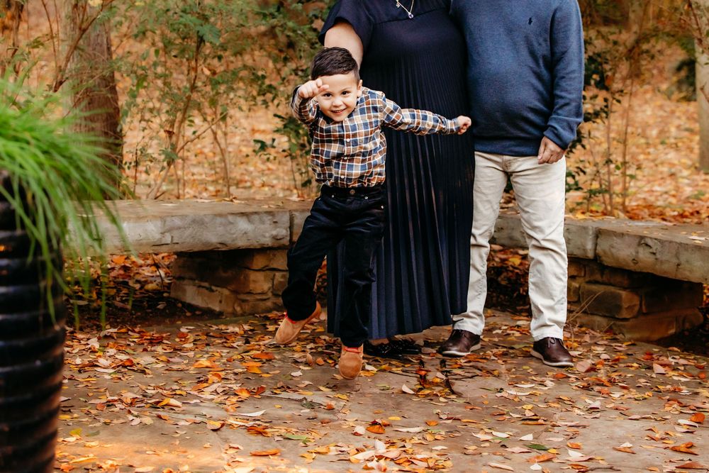A couple in casual fall attire poses together on a stone path covered in autumn leaves.