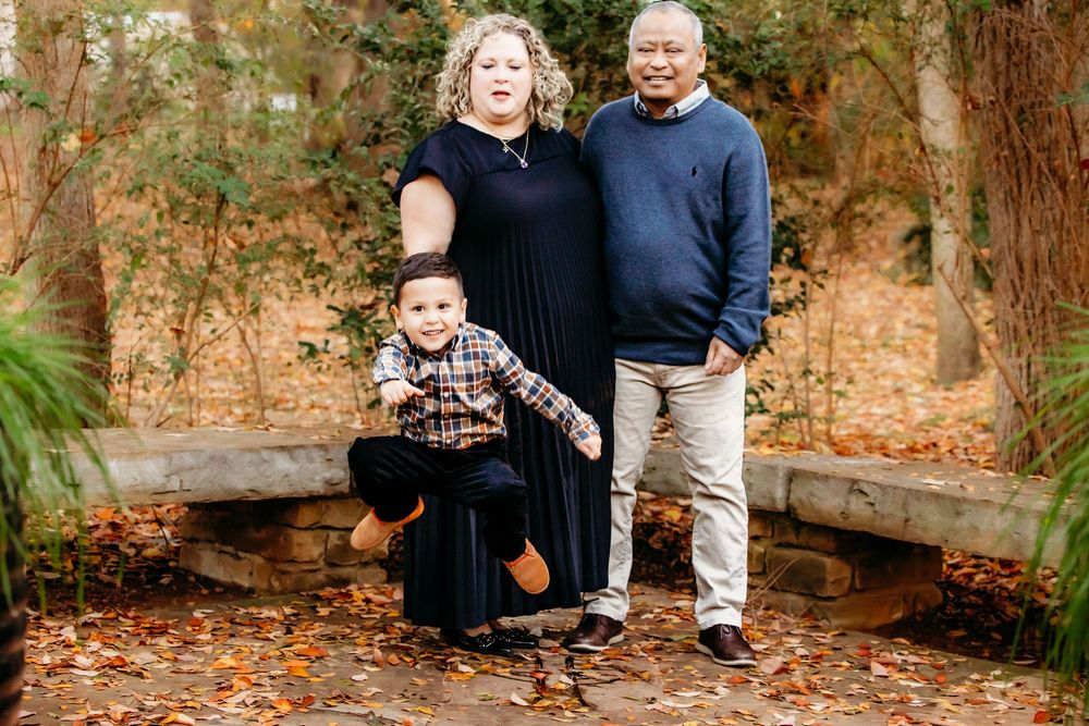 A family poses together on stone steps surrounded by autumn leaves in a wooded outdoor setting.
