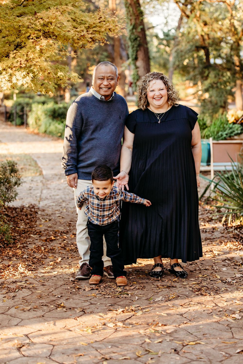 A couple sits together on brick steps surrounded by autumn foliage in an outdoor setting.